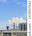 Industrial chemical plant facility with storage tanks and pipeline valve under a blue sky with cumulus clouds. 143897642