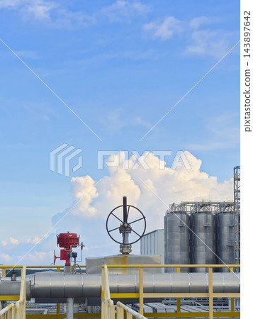 Industrial chemical plant facility with storage tanks and pipeline valve under a blue sky with cumulus clouds. 143897642