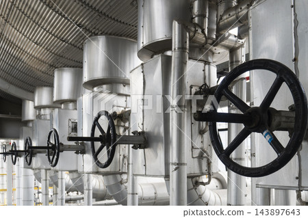 Row of large black valve handwheels on insulated industrial pipelines at a processing plant. Row of large black valve handwheels on insulated industrial pipelines at a processing plant. 143897643