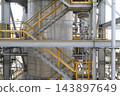 Industrial tank facility featuring complex steel structures and stairs with yellow safety handrails 143897649