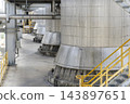 Close-up of large metal storage tanks and pipelines lined up in an industrial plant, featuring walkways with yellow safety railings. 143897651