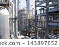 Wide view inside a large petrochemical refinery complex showing a dense network of insulated pipes, distillation columns, steel frames and yellow walkways representing the scale and complexity of 143897652