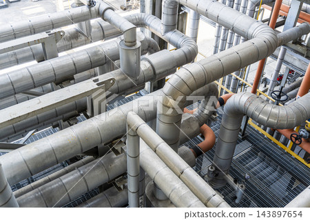 Intricate industrial metal pipeline system inside a factory facility Intricate industrial metal pipeline system inside a factory facility 143897654