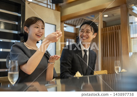 一對四十多歲的男女在吧台座位上吃壽司。 一對四十多歲的男女在吧台座位上吃壽司。 143897738