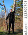 Young man performing side stretch in forest during outdoor workout 143899705