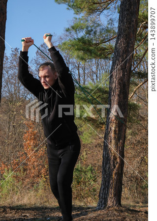 Young man using resistance band for strength training in forest Young man using resistance band for strength training in forest 143899707
