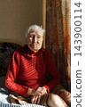 Old lonely woman sitting near the window in his house. 143900114