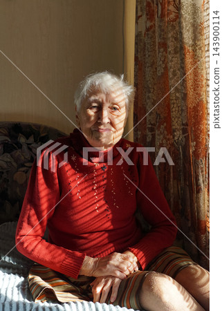 Old lonely woman sitting near the window in his house. 143900114