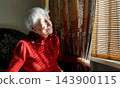 Old lonely woman sitting near the window in his house. 143900115