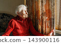 Old lonely woman sitting near the window in his house. 143900116