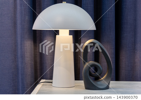 Modern interior lighting with a white lamp illuminating sculpture on a wooden table Modern interior lighting with a white lamp illuminating sculpture on a wooden table 143900370