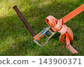 Ratchet strap secures cargo equipment to a metal stake on a grassy lawn 143900371