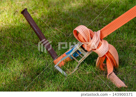 Ratchet strap secures cargo equipment to a metal stake on a grassy lawn Ratchet strap secures cargo equipment to a metal stake on a grassy lawn 143900371