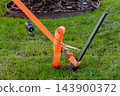 Ratchet strap secures cargo equipment to a metal stake on a grassy lawn 143900372