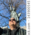 Man posing in front of a Statue of Liberty replica in Paris, France, on a sunny day. Travel, tourism and sightseeing concept. High quality photo 143900545