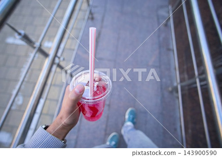Hand holding a transparent plastic cup of cold pink bubble tea or berry milkshake with black tapioca pearls and a straw Hand holding a transparent plastic cup of cold pink bubble tea or berry milkshake with black tapioca pearls and a straw 143900590