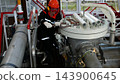 Industrial mechanic in safety gear tightens large machine assembly with hand tools, concentrated in industrial style facility. Mechanic works beside bolts, pipes, and insulated tubes on equipment. 143900645