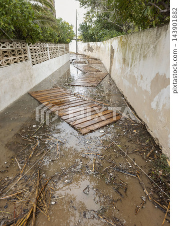 Flooded narrow street with submerged wooden boardwalk and debris Flooded narrow street with submerged wooden boardwalk and debris 143901882