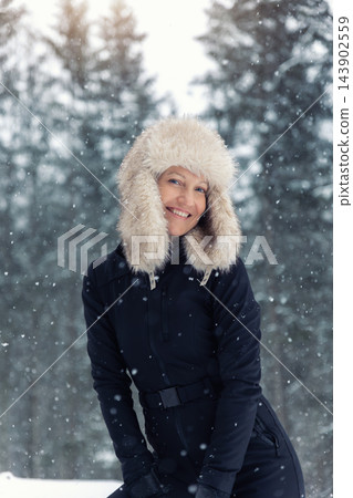 Portrait young adult mid age smile woman enjoy have fun walking in park forest snowfall cold winter day. Female portrait person happiness wear black ski overall stylish fur hat snowflakes background Portrait young adult mid age smile woman enjoy have fun walking in park forest snowfall cold winter day. Female portrait person happiness wear black ski overall stylish fur hat snowflakes background 143902559
