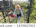 Cute little funny caucasian blond kid boy enjoy having fun walk metal net tunnel playground in treetop adventure amusement park Saarland. Children outdoors nature extreme sport activities concept 143902563