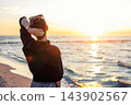 Back view young adult woman dreamy looking sunset horizon on sandy beach shore warm evening sunset light. Scenic wellbeing concept mindfulness balance hope emotional recovery mental health sea 143902567