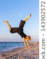 Active child performing handstand acrobatics on sandy beach during golden hour, showing balance, strength, flexibility, playful summer energy. Sea waves sunset light outdoor childhood fitness freedom 143902572