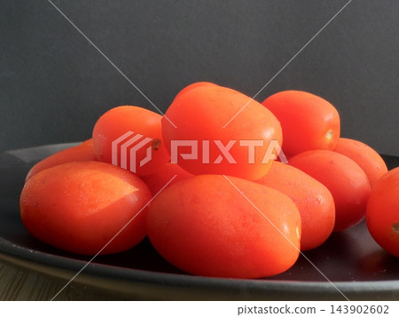 Fresh cherry tomatoes on a black plate. Fresh red tomatoes on a dark background. Fresh cherry tomatoes on a black plate. Fresh red tomatoes on a dark background. 143902602