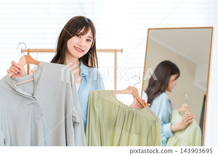 一位面帶微笑的女士正在從兩件襯衫中挑選一件。 143903695