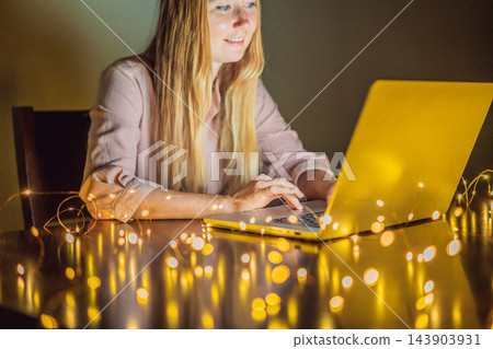 Woman using her home computer in the evening under warm string lights. 143903931