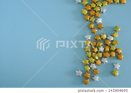 Glitter gold and silver origami lucky stars scattered on pastel blue background with copy space, ideal for festive celebrations Glitter gold and silver origami lucky stars scattered on pastel blue background with copy space, ideal for festive celebrations 143904695