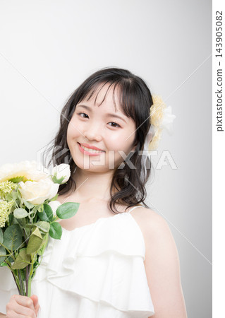 [白色背景] 一位二十多歲的日本年輕女子，身穿白色婚紗，手捧花束，以新娘的身份直視鏡頭。 143905082