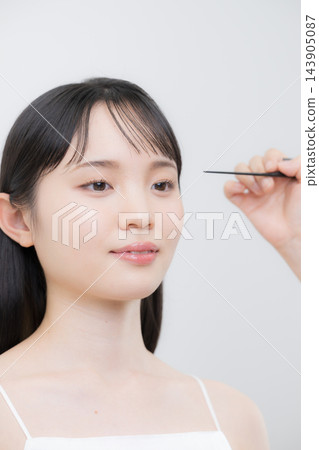 一位髮型師和化妝師正在梳理一位年輕日本女性的瀏海,示範如何打理她的瀏海以及如何打理她的頭髮。 一位髮型師和化妝師正在梳理一位年輕日本女性的瀏海,示範如何打理她的瀏海以及如何打理她的頭髮。 143905087