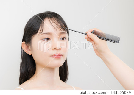 一位髮型師和化妝師正在梳理一位年輕日本女性的瀏海,示範如何打理她的瀏海以及如何打理她的頭髮。 一位髮型師和化妝師正在梳理一位年輕日本女性的瀏海,示範如何打理她的瀏海以及如何打理她的頭髮。 143905089