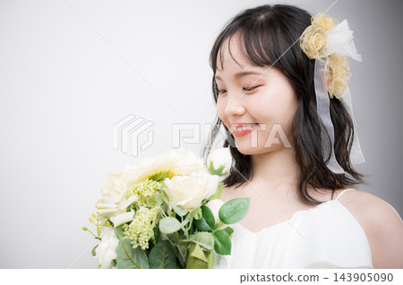[白色背景] 一位二十多歲的日本年輕女子，身穿白色婚紗，手捧花束，以新娘的身份直視鏡頭。 143905090