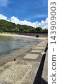 A view of a breakwater and sandy beach under a blue sky and summer cumulonimbus clouds. 143909003