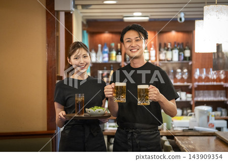 A smiling man and woman holding a beer mug and a tray - Izakaya/restaurant staff (image) A smiling man and woman holding a beer mug and a tray - Izakaya/restaurant staff (image) 143909354