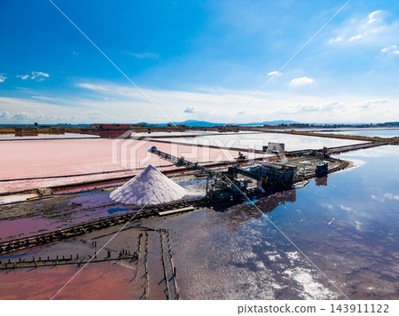 Salt extraction at a salt pond with a salt pile and machinery beside pink evaporation ponds under a blue sky Salt extraction at a salt pond with a salt pile and machinery beside pink evaporation ponds under a blue sky 143911122