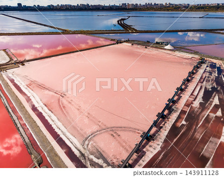 Salt extraction in broad evaporation ponds beside a coastal city, with pink brine and water channels visible from above Salt extraction in broad evaporation ponds beside a coastal city, with pink brine and water channels visible from above 143911128