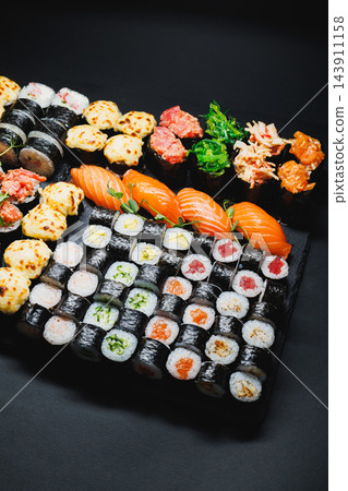 Assorted sushi rolls and nigiri arranged on a black platter for a meal Assorted sushi rolls and nigiri arranged on a black platter for a meal 143911158