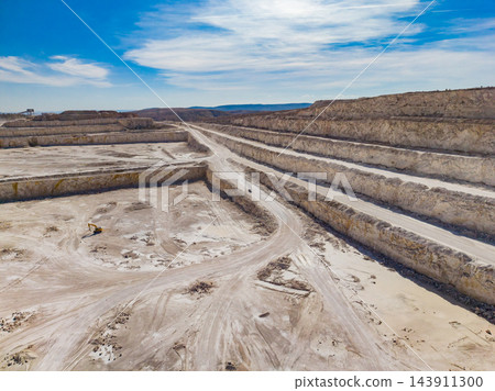 Terraced quarry excavation with haul roads crossing the mine floor under a cloudy sky 143911300