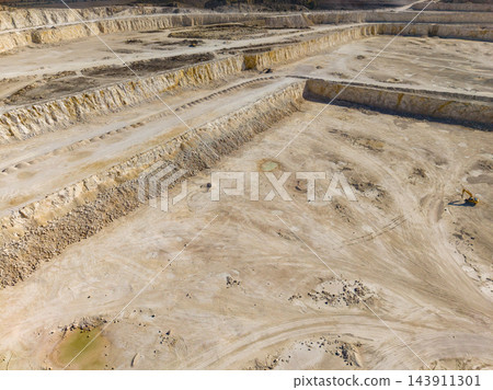 Terraced quarry excavation with haul roads and machinery working across the exposed pit floor 143911301