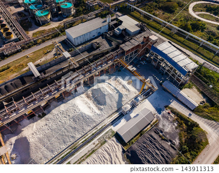 Aerial view of an industrial processing plant with storage piles and pipe systems during daylight Aerial view of an industrial processing plant with storage piles and pipe systems during daylight 143911313