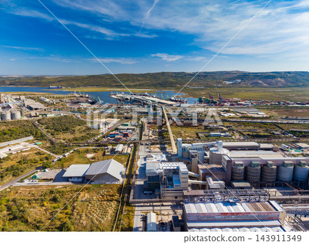Industrial plant and port facilities along the coast near a low range of hills under a wide sky Industrial plant and port facilities along the coast near a low range of hills under a wide sky 143911349