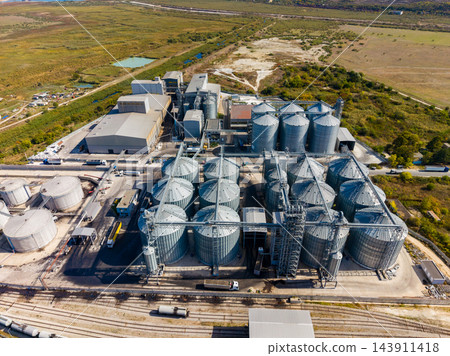 Aerial view of an industrial grain storage and processing facility beside rail tracks in a rural area 143911418