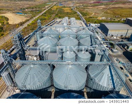 Aerial view of grain storage silos and processing equipment at an industrial facility beside rail tracks Aerial view of grain storage silos and processing equipment at an industrial facility beside rail tracks 143911443