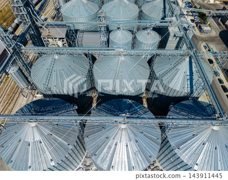 Aerial view of grain silos and conveyor structures at an agricultural storage facility during daylight Aerial view of grain silos and conveyor structures at an agricultural storage facility during daylight 143911445