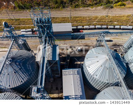 Grain silos and conveyor equipment beside freight rail tracks at an agricultural storage facility in daylight Grain silos and conveyor equipment beside freight rail tracks at an agricultural storage facility in daylight 143911449