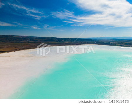 Chemical waste contaminates a turquoise water basin beside a pale shore under a cloudy sky Chemical waste contaminates a turquoise water basin beside a pale shore under a cloudy sky 143911473