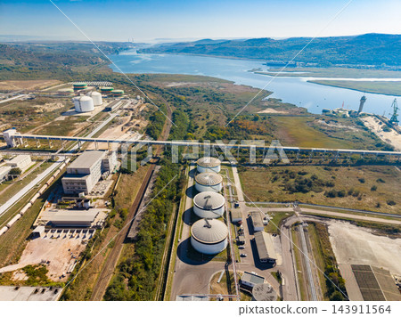 Aerial view of storage tanks and industrial facilities beside a coastal inlet during daylight 143911564