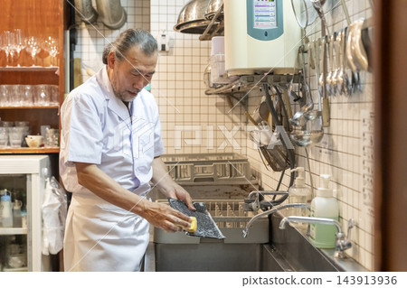 一位老年男子在餐廳廚房洗碗 一位老年男子在餐廳廚房洗碗 143913936